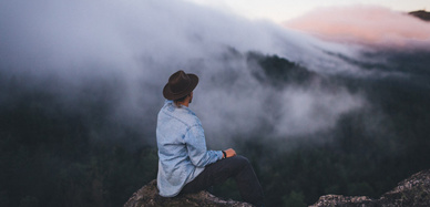 Wanderer auf Felsen vor nebligen, bewaldeten Hängen
